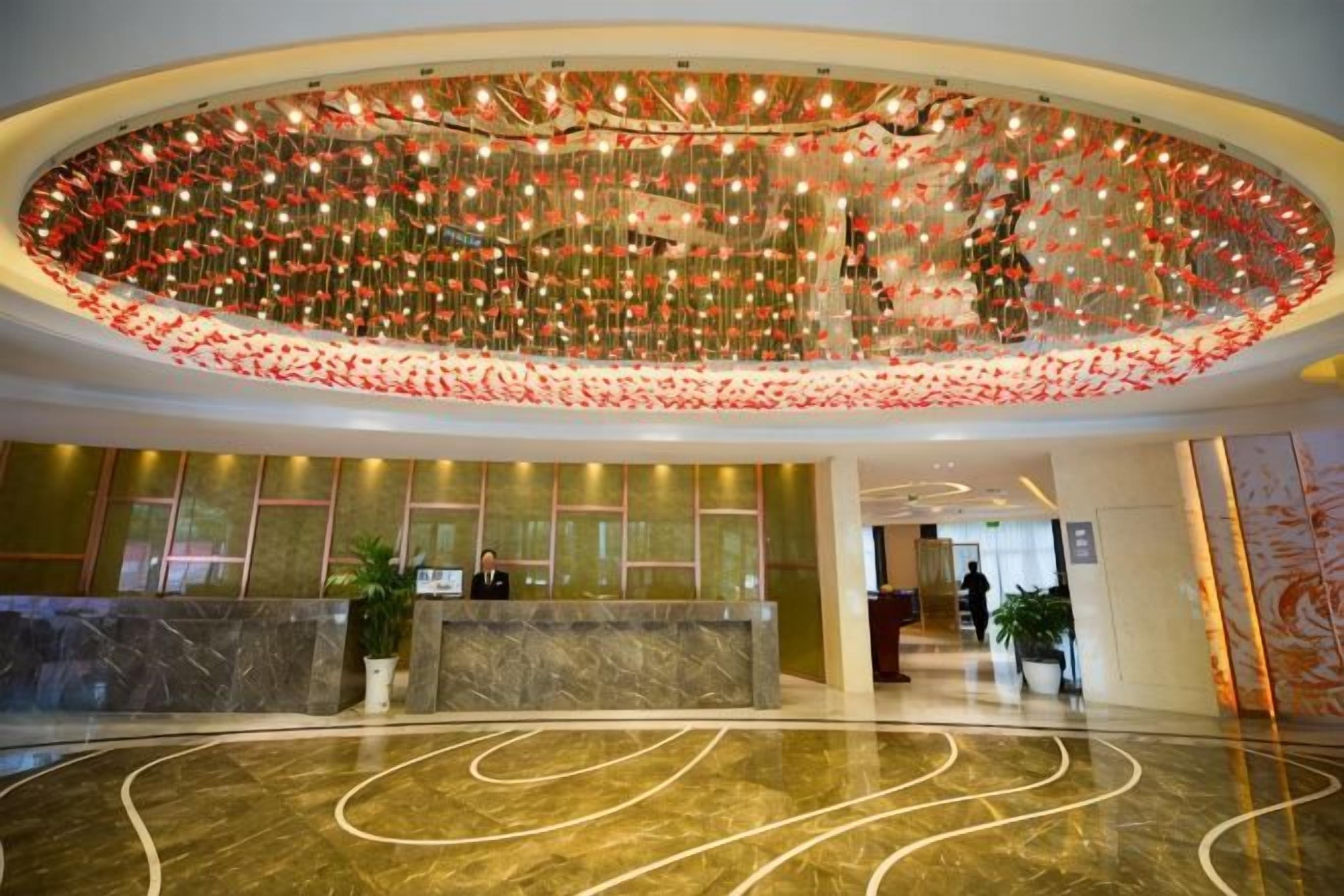 A hotel lobby with a marble reception desk, a large decorative ceiling, and a curved floor design.
