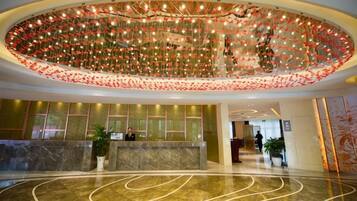 A hotel lobby with a marble reception desk, a large decorative ceiling, and a curved floor design.