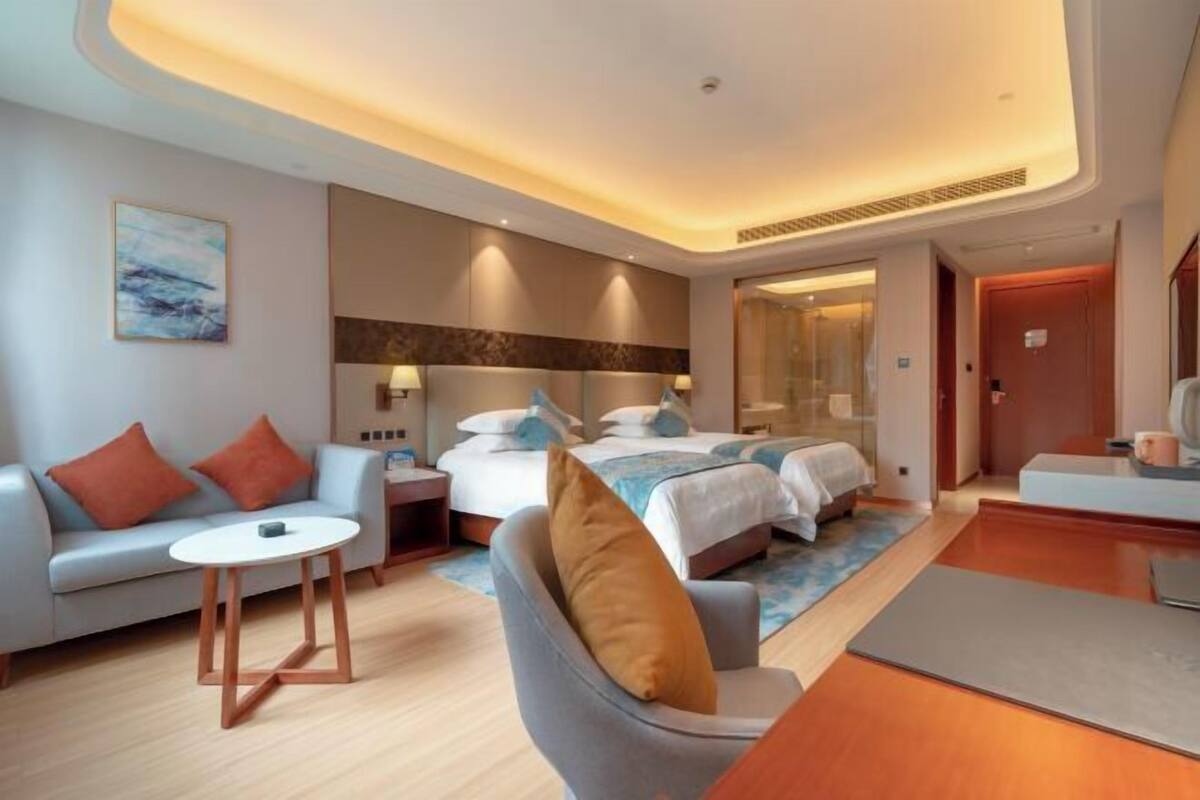 A modern hotel room with a sofa, two beds, a small table, and a desk.