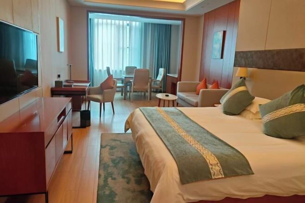 Habitación de hotel con cama, televisión, escritorio y zona de estar con sillas y mesa.