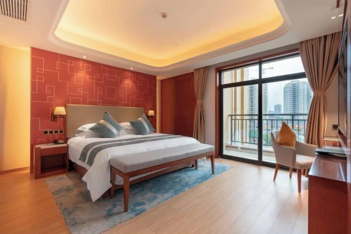 A modern hotel room with a large bed, a desk, and a view of the city.