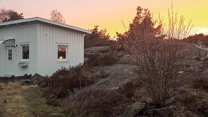 Ein weißes Gebäude mit kleinem Fenster, umgeben von felsigem Gelände und spärlicher Vegetation.