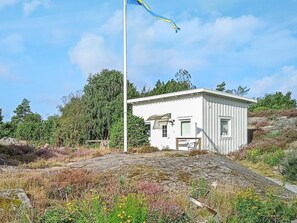 A small white building with a flagpole, surrounded by natural vegetation and a stone pathway. - 4 Person Holiday Home in Kyrkesund (Kyrkesund)