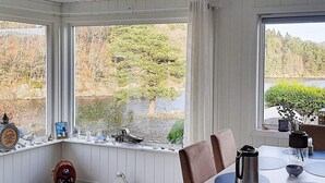 A dining area with a view of a lake and forest, featuring a table with chairs, a lantern, and a birdcage. - 9 Person Holiday Home in Lyngdal (Lyngdal)