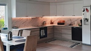 A modern kitchen with a dining area, featuring a marble countertop, built-in cabinets, and a stainless steel refrigerator. - 9 Person Holiday Home in Lyngdal (Lyngdal)