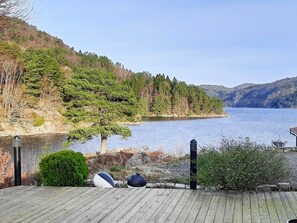 A wooden deck overlooking a lake with trees and hills in the background. - 9 Person Holiday Home in Lyngdal (Lyngdal)