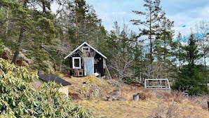 A small cabin with a sloped roof, surrounded by dense forest and a grassy area. - 5 Person Holiday Home in Tyreso (Tyreso)