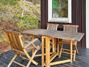 A wooden deck with a table and chairs, a window, and a view of a hillside. - 5 Person Holiday Home in Tyreso (Tyreso)