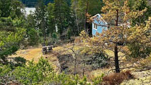 A cabin with a blue exterior, surrounded by dense forest and a lake in the background. - 5 Person Holiday Home in Tyreso (Tyreso)