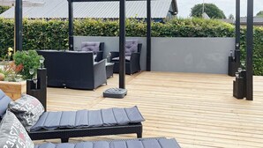 Un patio exterior con mobiliario de mimbre, cojines y una estructura de pérgola.
