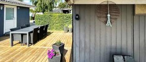 A wooden deck with outdoor furniture, a small planter with flowers, and a hanging light fixture.