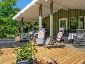 A covered outdoor seating area with wicker chairs and a table, surrounded by greenery. - 4 Star Holiday Home in Ulfborg (Ulfborg)