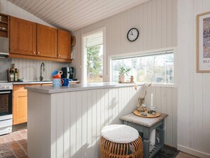 A kitchen with wooden cabinets, a white countertop, a clock, and a window with a view of greenery. - 4 Star Holiday Home in Ulfborg (Ulfborg)