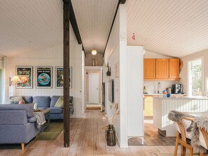 A cozy living room with a sofa, a dining area with wooden cabinets, and a kitchen with a coffee machine. - 4 Star Holiday Home in Ulfborg (Ulfborg)