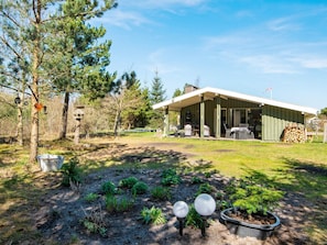 A modern house with a covered porch, a garden with various plants, and a stack of firewood. - 4 Star Holiday Home in Ulfborg (Ulfborg)