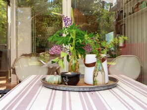 Une table à manger recouverte d’une nappe à rayures, un plateau rond avec une citrouille, un bol noir et deux vases avec des plantes.