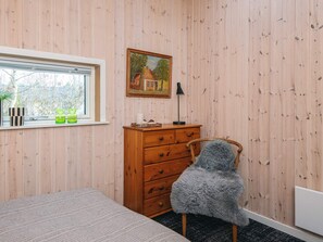 Une chambre avec une commode en bois, une chaise, un lit, une fenêtre donnant sur un beau paysage et un tableau accroché au mur.