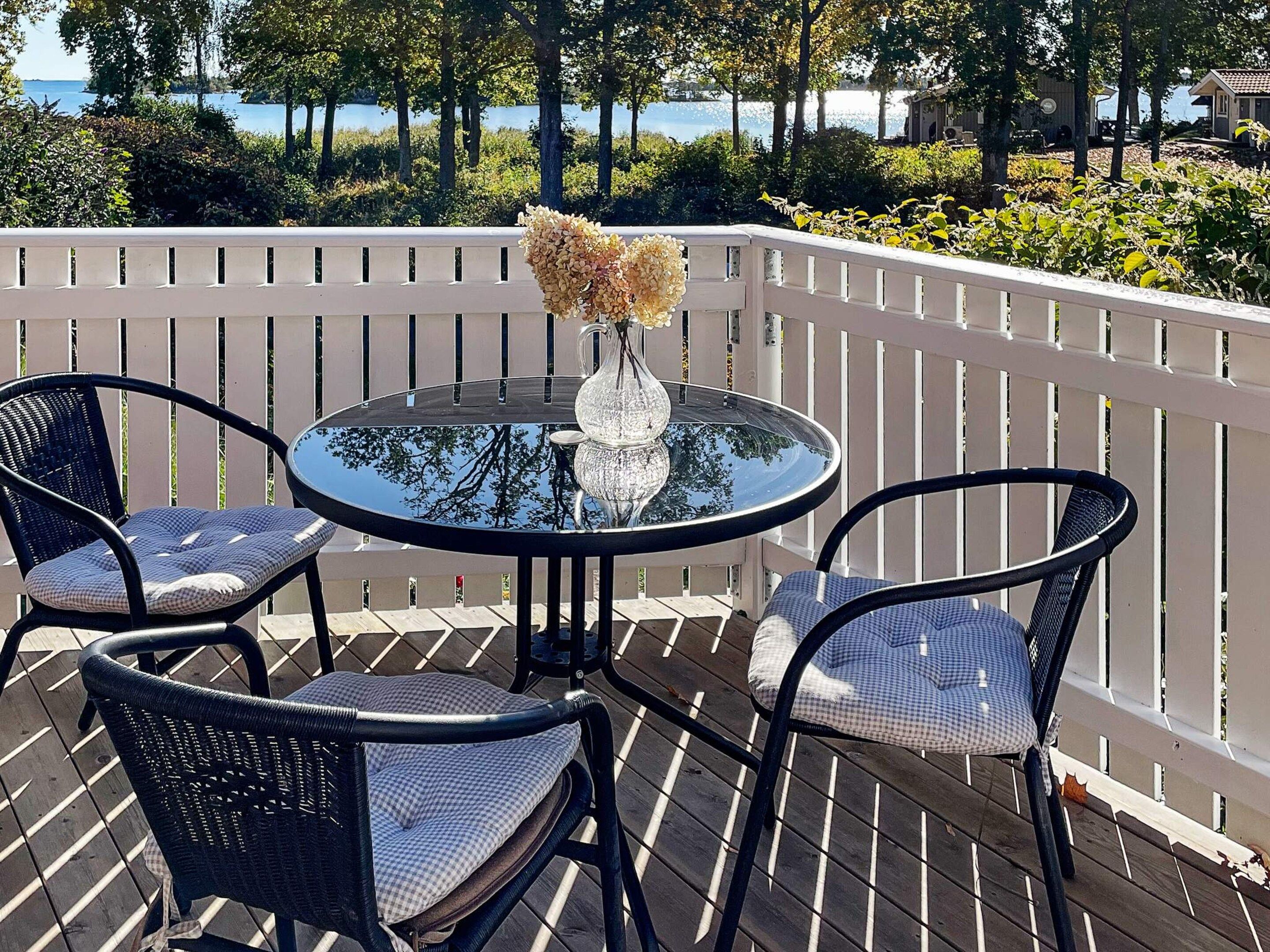 A round table with a glass top, surrounded by two wicker chairs with cushions, set on an outdoor deck with a white railing.
