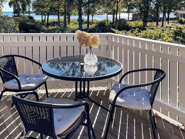 A round table with a glass top and a vase with dried flowers, surrounded by two wicker chairs with cushions.