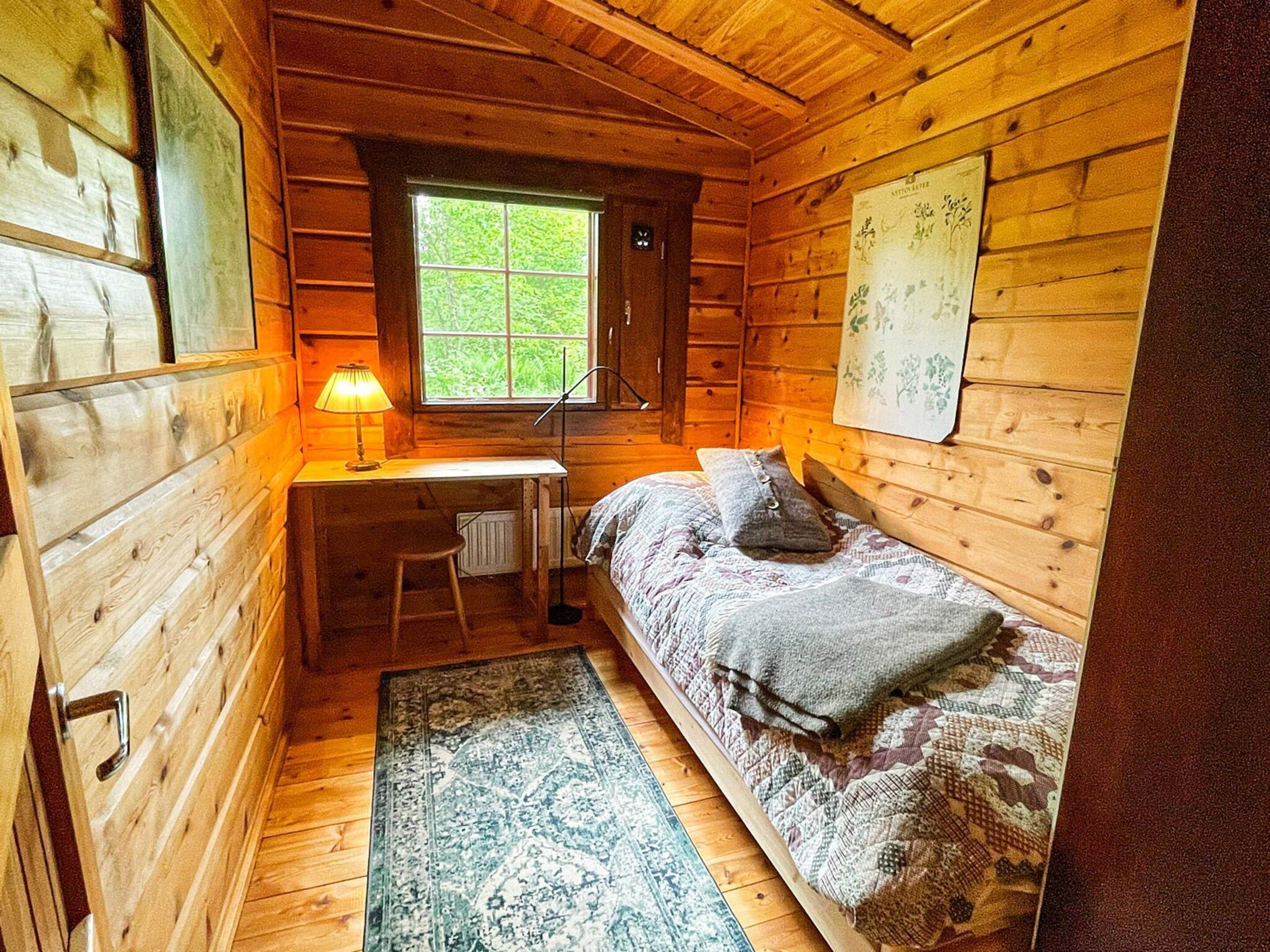 A compact wooden cabin room with a single bed, a desk, and a window.