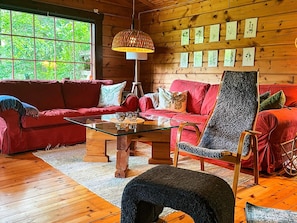 A cozy cabin interior with a red sofa, a glass coffee table, a patterned armchair, and a wooden floor. - 6 Person Holiday Home in Blentarp (Blentarp)