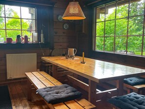 A wooden dining table with benches, a hanging lamp, and a view of greenery outside.