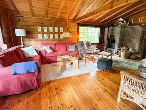 A cozy cabin interior with a wooden ceiling, a red sofa set, a wicker chair, a glass coffee table, and a brick fireplace. - 6 Person Holiday Home in Blentarp (Blentarp)