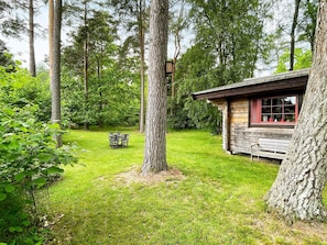 A rustic cabin with a wooden exterior, a bench, and a dining table set outdoors surrounded by trees. - 6 Person Holiday Home in Blentarp (Blentarp)