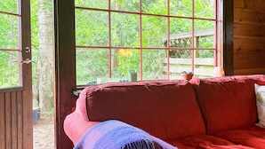 A red sofa with a blue throw blanket, a wooden door, and a view of greenery outside. - 6 Person Holiday Home in Blentarp (Blentarp)