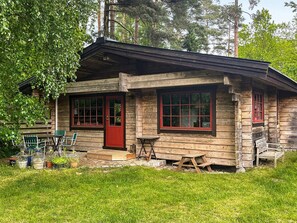 A rustic wooden cabin with a red door and windows, a small porch, and a table with chairs. - 6 Person Holiday Home in Blentarp (Blentarp)