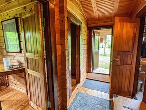 A wooden cabin interior with a desk, a chair, and a door leading outside.