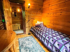 A wooden cabin room with a bed, a desk, and a mirror.