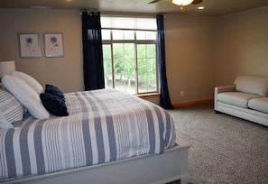 A bedroom with a bed, a window with curtains, a sofa, and two framed pictures on the wall.