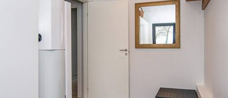 A hallway with a white door, a small bench, and a mirror on the wall.