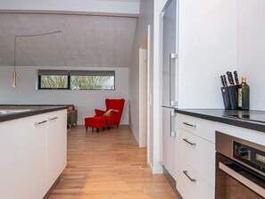 A modern kitchen with white cabinets, a red chair, and a window with a view of trees. - 8 Person Holiday Home in Aabenraa (Aabenraa)