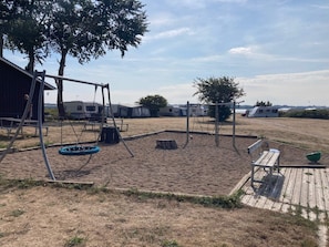 A sandy outdoor area with a swing set, picnic table, and a wooden deck. - 8 Person Holiday Home in Aabenraa (Aabenraa)