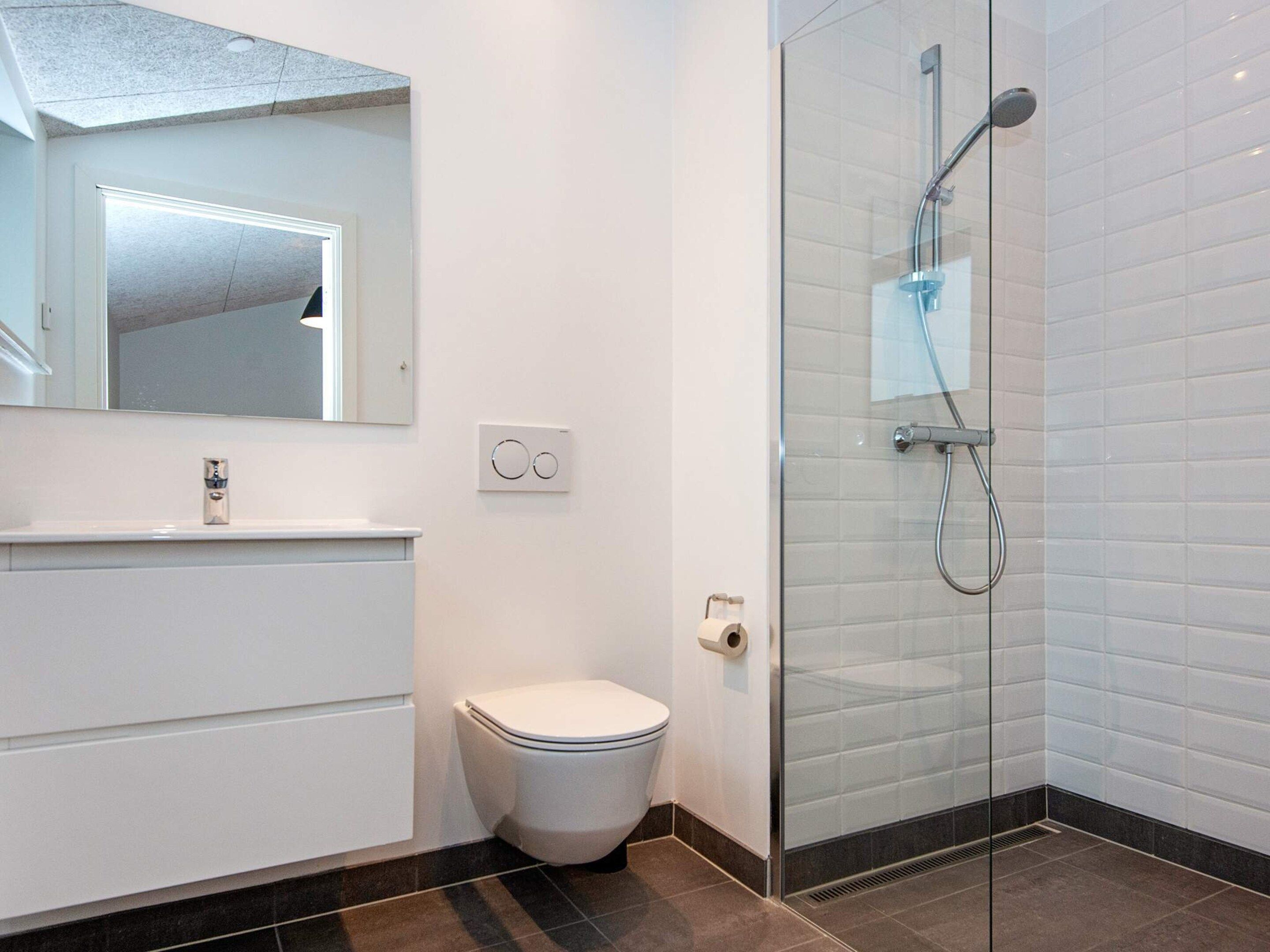A modern bathroom with a toilet, a glass-enclosed shower, and a white sink with a mirror above it.