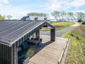 Eine Holzdar Terrasse mit Sitzgelegenheiten im Freien und einem überdachten Bereich, mit Blick auf einen See und ein Haus im Hintergrund.