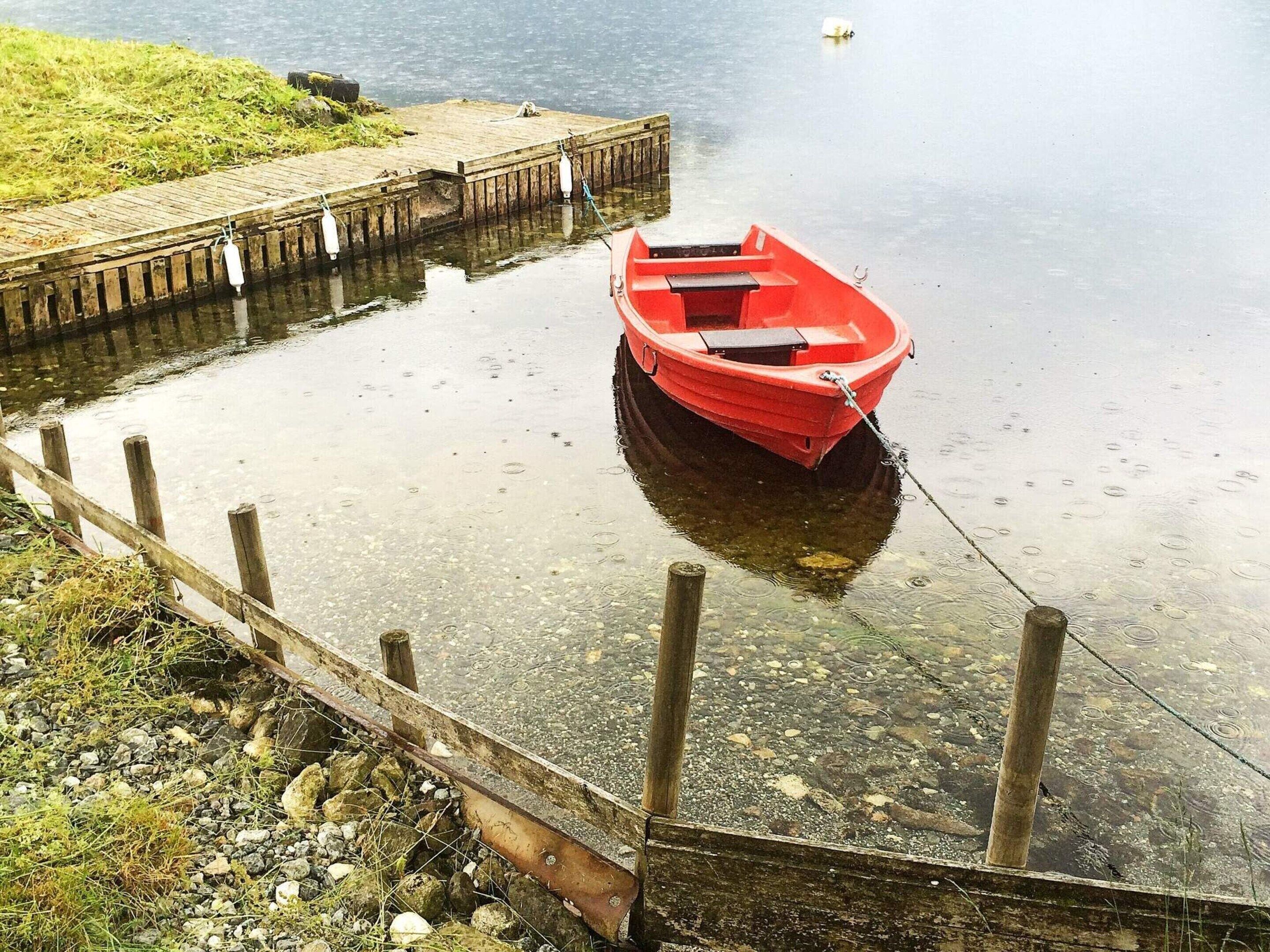 A red boat tied to a wooden dock extending into calm water.