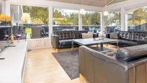 Un espacio exterior moderno con un sofá modular, una mesa de comedor y vistas al jardín trasero.