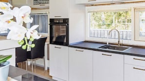 Cocina moderna con armarios blancos, un horno negro y un ventanal con vistas al verdor.