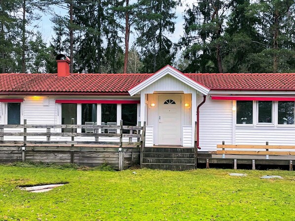 A white building with a red roof, a wooden deck, and a small porch. - 4 Star Holiday Home in Prassebo (Prässebo)