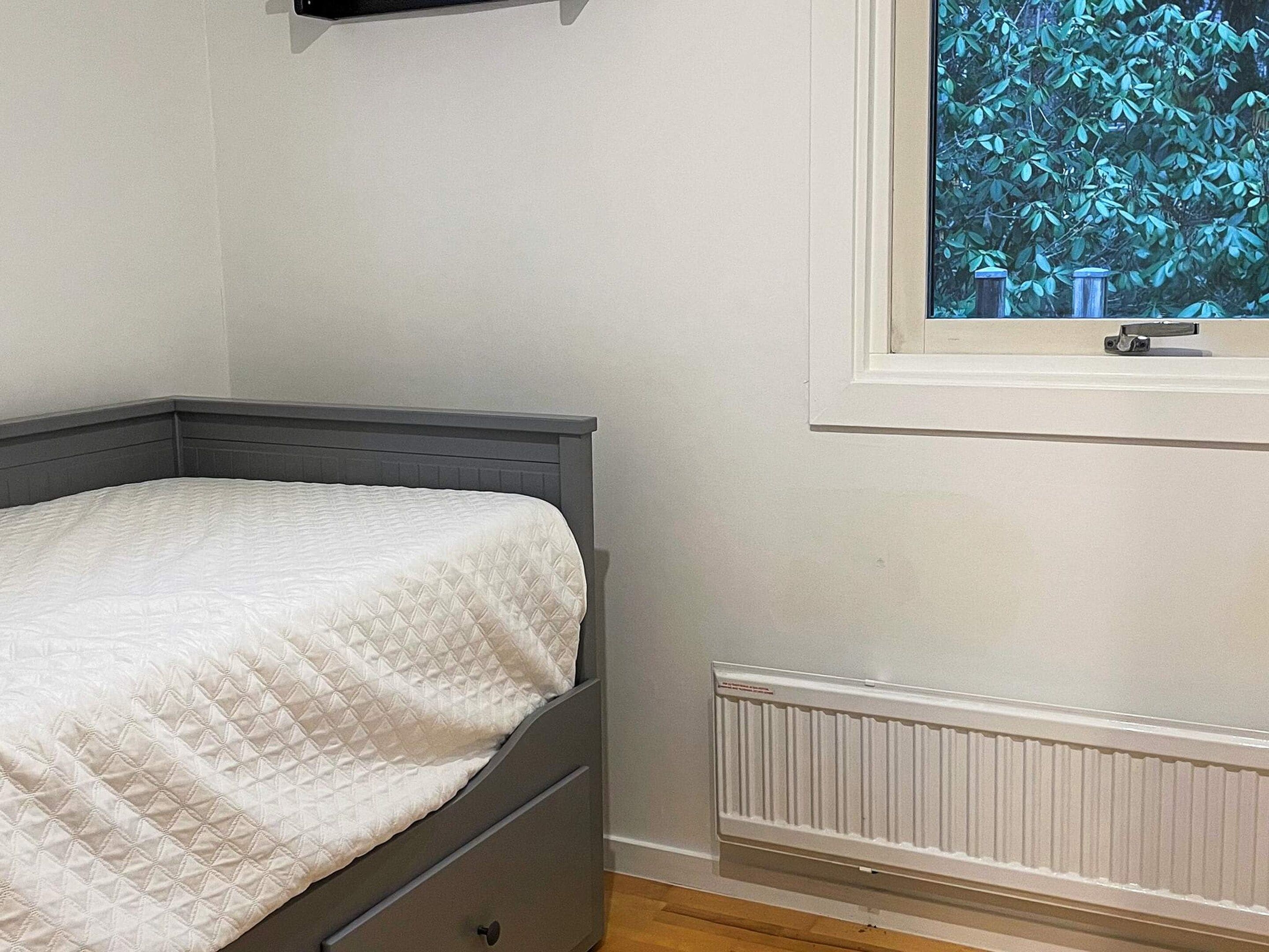 Un dormitorio con cama, ventana y vistas a la vegetación, y un radiador.