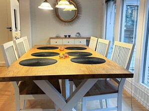 A dining table with black placemats, white chairs, and pendant lights.