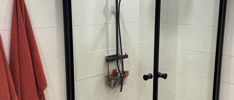 Een douchecabine met glazen wanden, een handdouche, een wandmengkraan en een zeepbak met flessen.