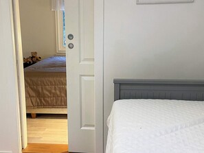 A bedroom with a bed, a door leading to another room, and a window with curtains.