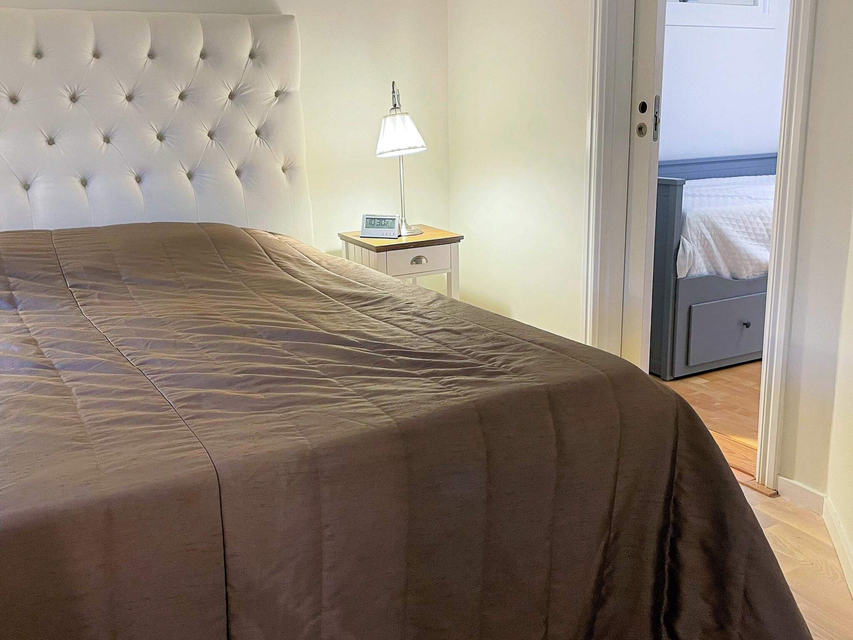 A bedroom with a tufted headboard, a bedside table with a lamp, and a bed with a brown bedspread.
