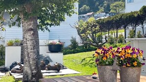 A backyard with a wooden deck, a large tree, and two flower pots with colorful flowers. - 4 Star Holiday Home in Maloy (Kinn)