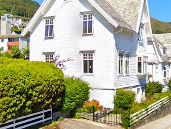 A white two-story house with a steep roof, surrounded by greenery and a white fence. - 4 Star Holiday Home in Maloy (Kinn)