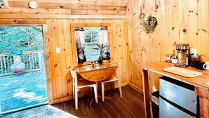A wooden cabin interior with a dining table, chairs, a coffee maker, and a refrigerator.